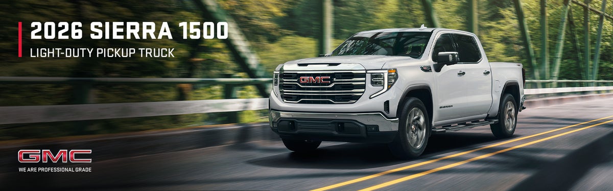 2026 GMC Sierra 1500 light-duty pickup truck driving across a forest bridge
