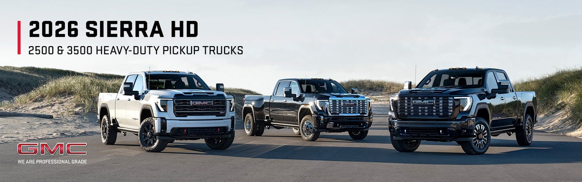 Three 2026 GMC Sierra HD heavy-duty pickup trucks parked among beach dunes
