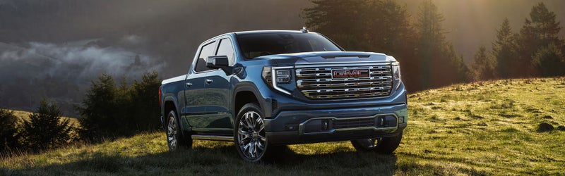 Blue 2026 GMC Sierra 1500 Denali parked on a misty hillside at sunrise