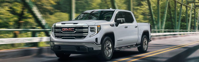 White 2026 GMC Sierra 1500 driving across a tree-lined bridge