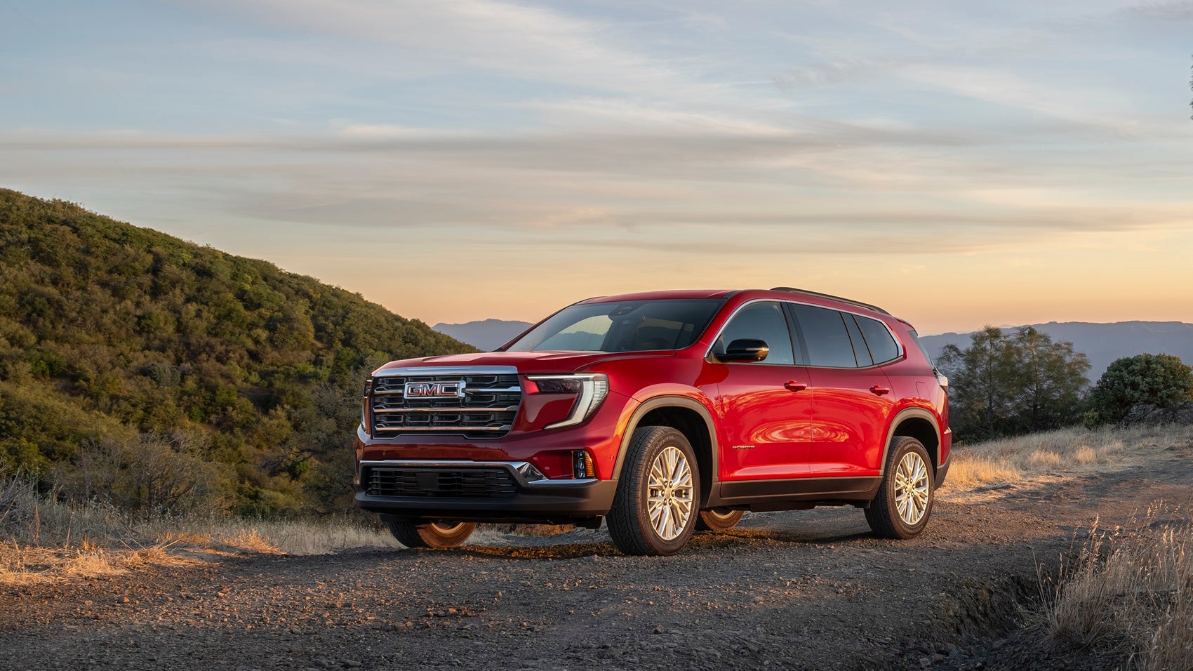 Red GMC Acadia parked in a hill-like area at sunset